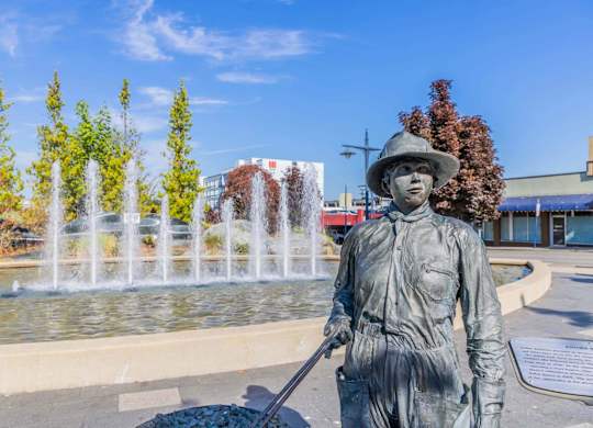 A statue of a person holding a shovel stands in front of a fountain.