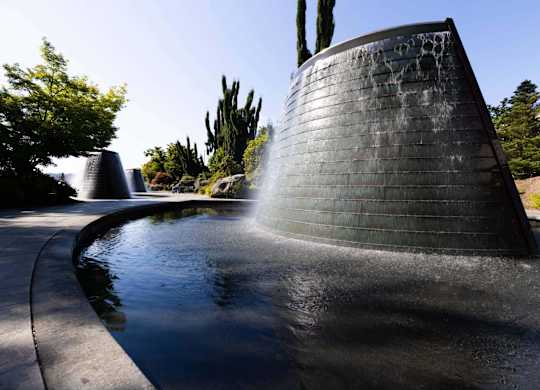 A water feature in a park with a tall, black, cylindrical structure.