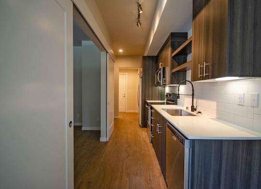 A modern kitchen with dark wood floors and white countertops at B Flats Apartments, Bremerton, 98337