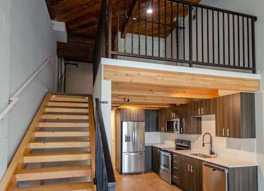 A wooden staircase with a metal railing leads to a kitchen area at B Flats Apartments, Washington
