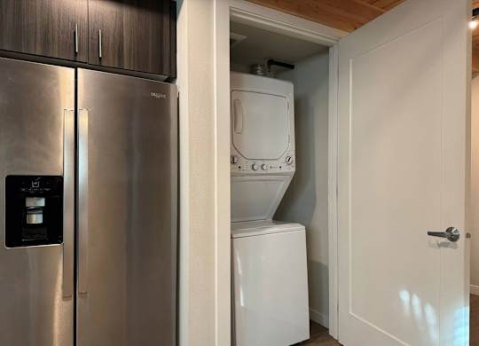 A stainless steel refrigerator is next to a white washing machine in a kitchen at B Flats Apartments, Bremerton, 98337