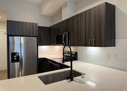 A modern kitchen with dark wood cabinets and a stainless steel refrigerator at B Flats Apartments, Bremerton, Washington