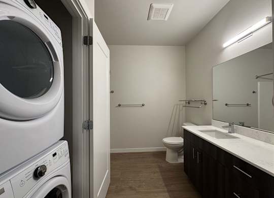 A white washing machine is in a small laundry room with a toilet and sink at B Flats Apartments, Bremerton, WA