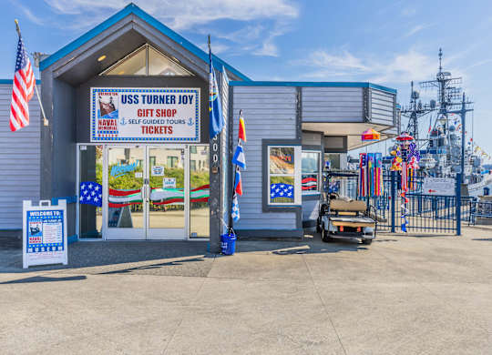 A gift shop named USS Turner Joy is located in front of a fence.