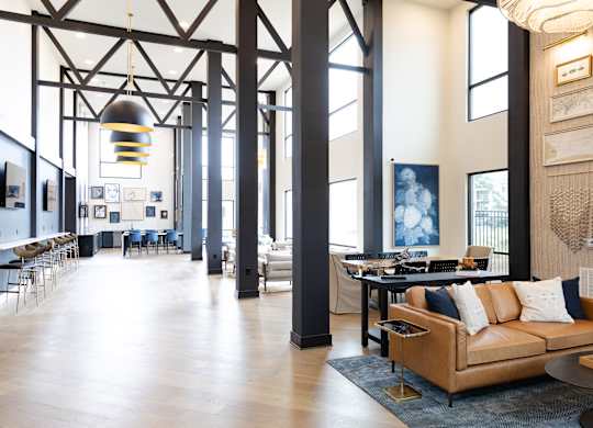 Industrial loft style lobby with exposed beams and leather sofa at The Crest at South Point Apartments, McDonough, Georgia