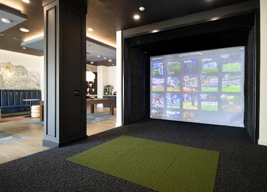 Golf simulator with projection screen and hitting mat at The Crest at South Point Apartments, McDonough, GA 30253