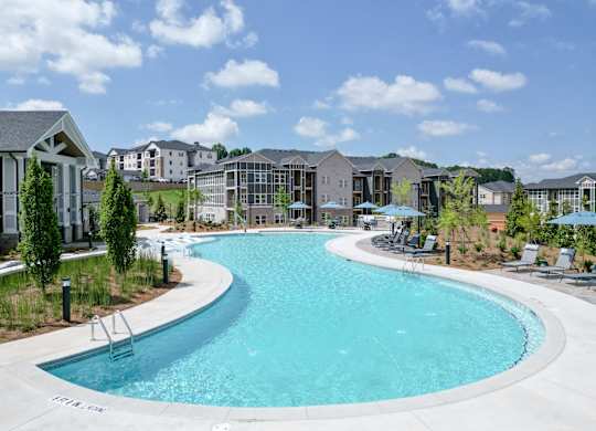 A large outdoor swimming pool surrounded by lounge chairs and umbrellas. at The Crest at Oakwood Apartments, Georgia