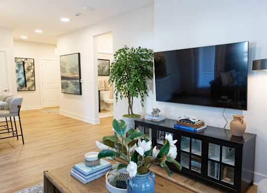 Two-bedroom model apartment area with wood-look flooring and a wall-mounted TV at The Crest at Oakwood in Oakwood, GA.