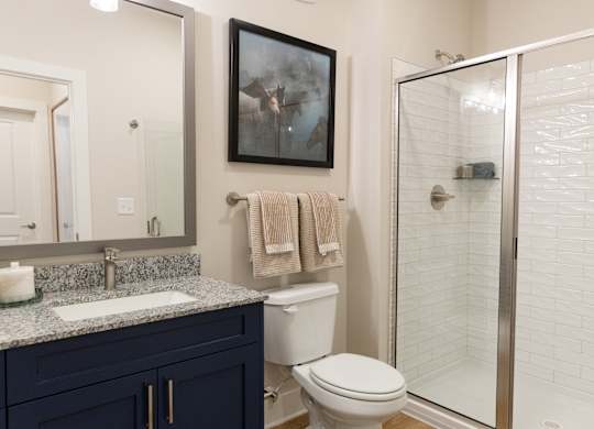 Secondary bathroom with a glass-encoder shower and navy vanity in a two-bedroom apartment at The Crest at Oakwood in Oakwood, GA.