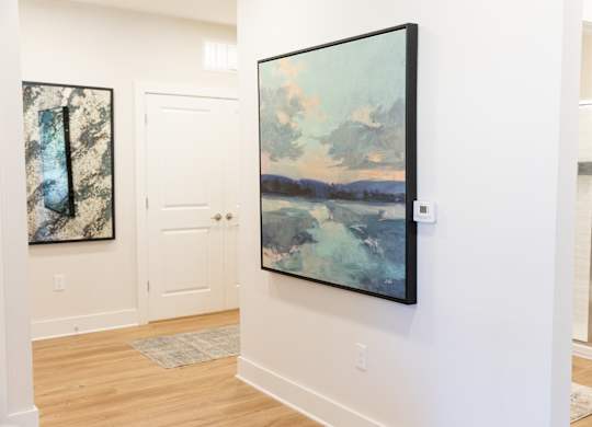 Hallway with wood-look flooring and frames artwork in a two-bedroom model apartment at The Crest at Oakwood in Oakwood, GA.