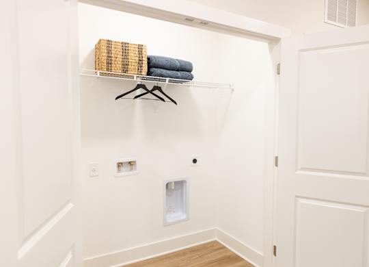 Laundry closet with washer and dryer hookups and overhead shelving in a two-bedroom apartment at The Crest at Oakwood in Oakwood, GA.