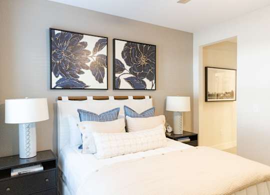 Primary bedroom with a staged bed, bedside tables and framed artwork in a two-bedroom model apartment at The Crest at Oakwood in Oakwood, GA.