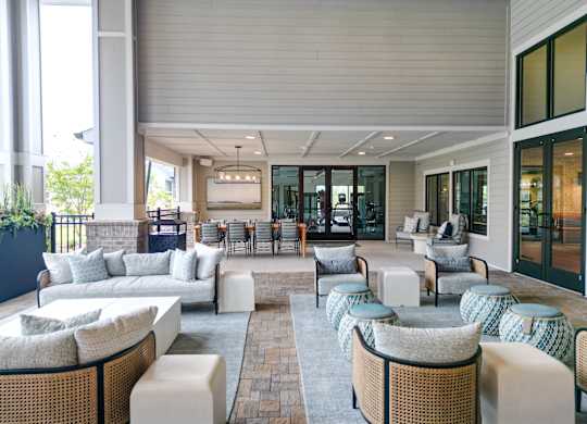 Covered outdoor clubhouse seating area with sofas and lounge chairs at The Crest at Oakwood apartments in Oakwood, GA.