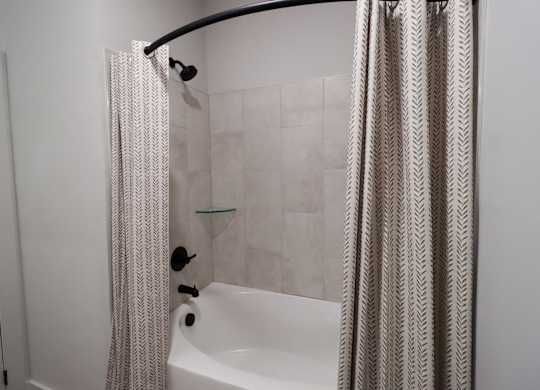 Bathroom with tub shower combo and patterned curtain at The Crest at South Point Apartments, McDonough, 30253