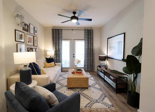 Living room with ceiling fan and patterned area rug at The Crest at South Point Apartments, McDonough, Georgia