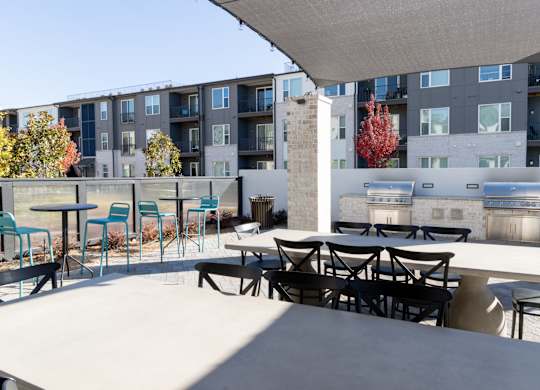 Outdoor grilling area with dining tables and shade canopy at The Wren Apartments, Georgia, 30043