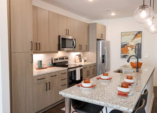 Modern kitchen with granite countertop and light wood cabinets at The Wren Apartments, Lawrenceville, GA