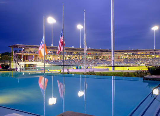 a view of a swimming pool, flags and a stadium in the background