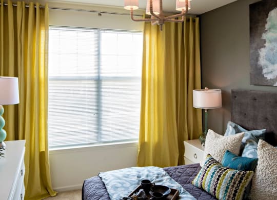 a bedroom with yellow curtains and a window at Reveal Hackensack apartments