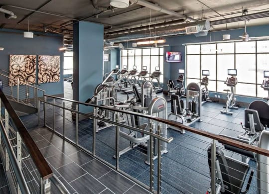 a gym with cardio machines and large windows at Reveal Hackensack apartments