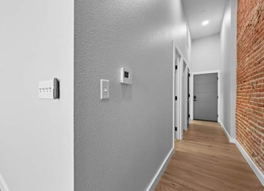 A hallway with a brick wall on the side and a door at the end at The Avenue Lofts Golden Apartments, Golden, Colorado