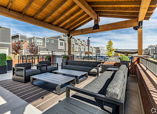 A wooden pergola with resident lounge, including black furniture and a striped rug.