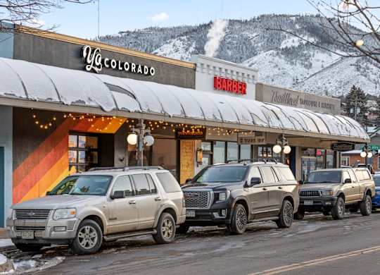 A row of SUVs are parked in front of a barber shop and a yoga studio at The Avenue Lofts Golden Apartments, Colorado, 80401