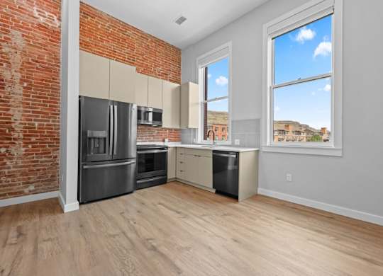 A kitchen with a brick wall and wooden floors at The Avenue Lofts Golden Apartments, Golden, CO