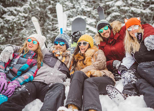 A group of friends are sitting in the snow with their skis and snowboards.