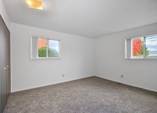 A room with a carpeted floor and two windows.