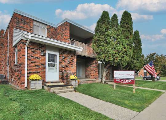 A brick house with a porch and a sign in front of it.