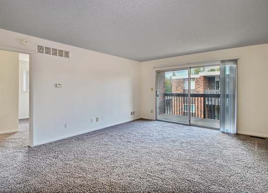 A spacious room with a grey carpet and a sliding glass door leading to a balcony.