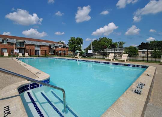 Outdoor swimming pool with sunchairs at Warren Woods Apartments in Warren, MI.