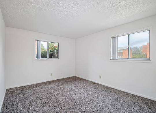 A room with two windows and carpeted floor.