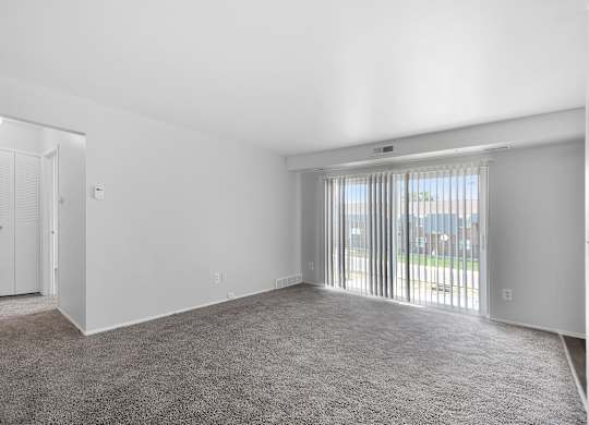 Spacious living room with large windows, neutral walls, and plush carpet at Warren Woods Apartments in Warren, MI.