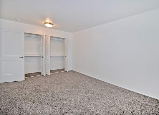 Comfortable bedroom at Woodcrest Apartments in Westland, MI featuring soft carpet flooring, a large closet, and peaceful natural light.
