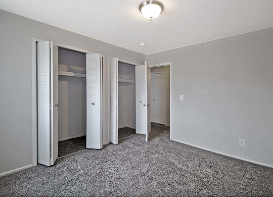 Bright bedroom with large closet, neutral paint, and soft carpeting at Warren Woods Apartments in Warren, MI.