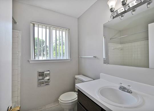 Bathroom with white vanity, framed mirror, and shower-tub combo at Warren Woods Apartments in Warren, MI.