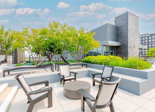 A patio with chairs and a table is surrounded by trees.