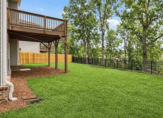A backyard with a wooden deck and a black fence.