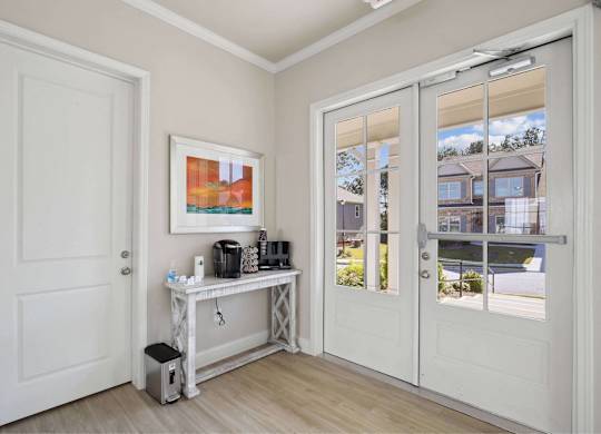 A white door is open to a room with a table and a painting on the wall.