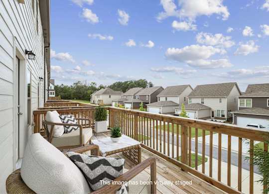 A balcony with a white couch and pillows overlooks a residential street.