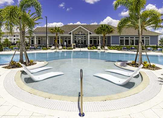 a large swimming pool with white chairs and a building in the background