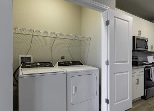 a washer and dryer in a laundry room with a kitchen in the background