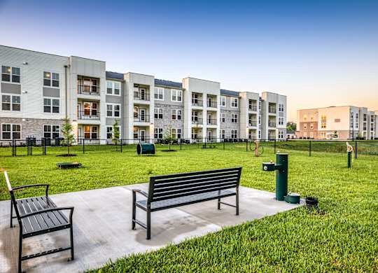 A park with benches and grass in front of apartment buildings.