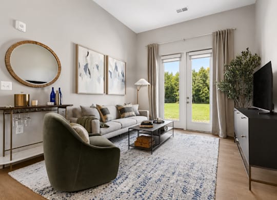 A living room with a grey couch, a round mirror, a coffee table, and a flat screen TV.
