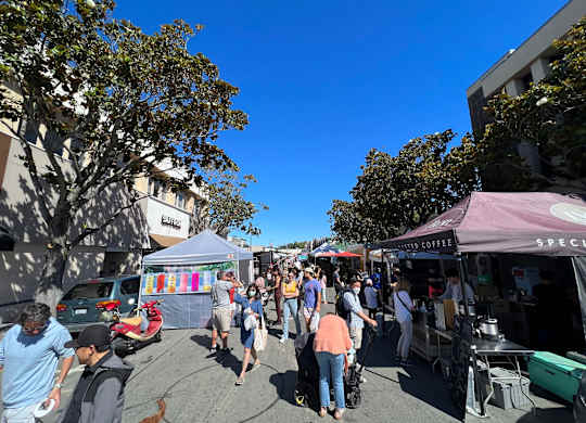 A busy outdoor market with people walking around and various stalls.