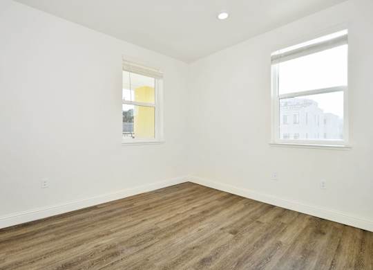an empty room with wood floors and two windows