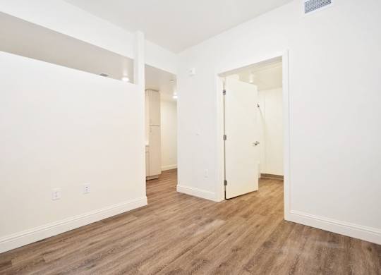 A room with white walls and wood flooring with a door on the right.