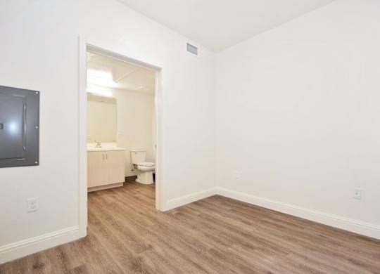 A room with a wooden floor and a white wall with a doorway leading to another room.